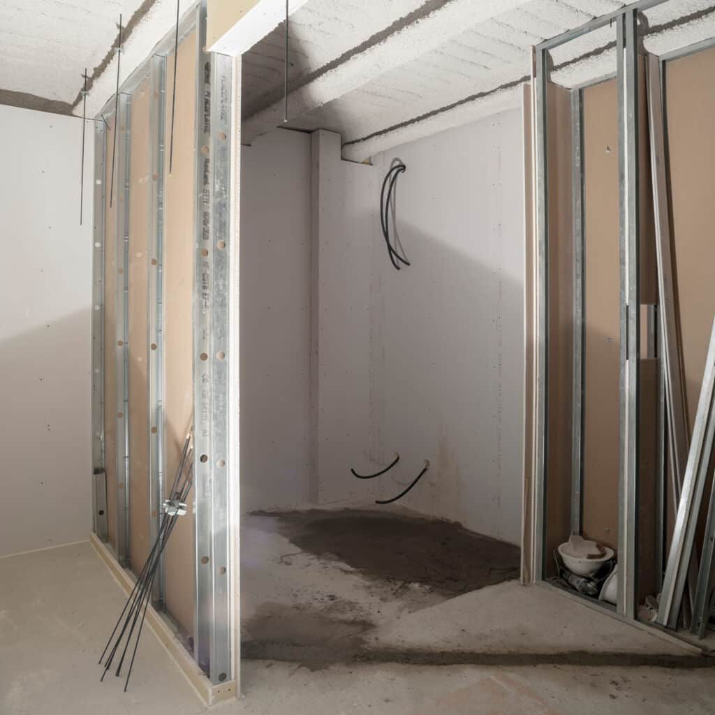 Montage de cloisons Placo sur ossature métallique en chantier Chantier de cloisonnement : ossature métallique, plaques de plâtre Placo et gaines électriques sur mur en béton.